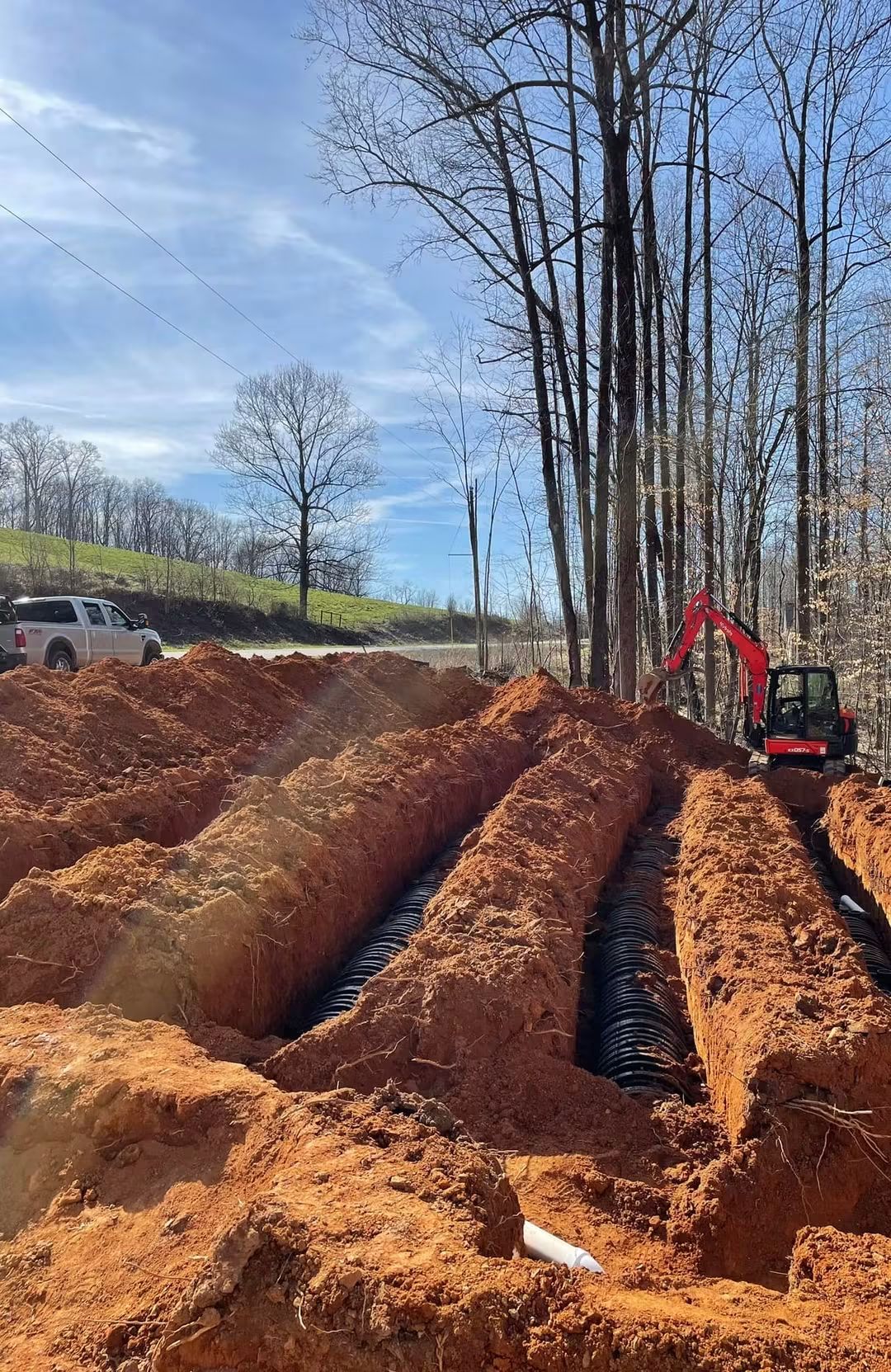 Excavated drainfield trenches with chamber pipe and a compact excavator on site