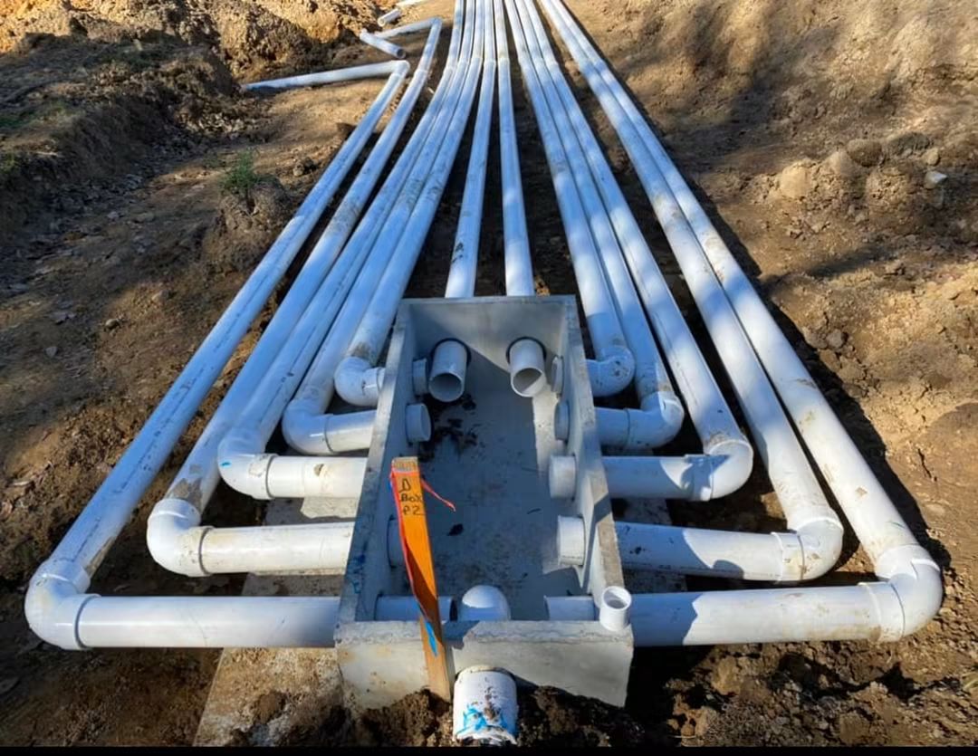 Force main manifold and PVC header assembly set in an open trench before backfill