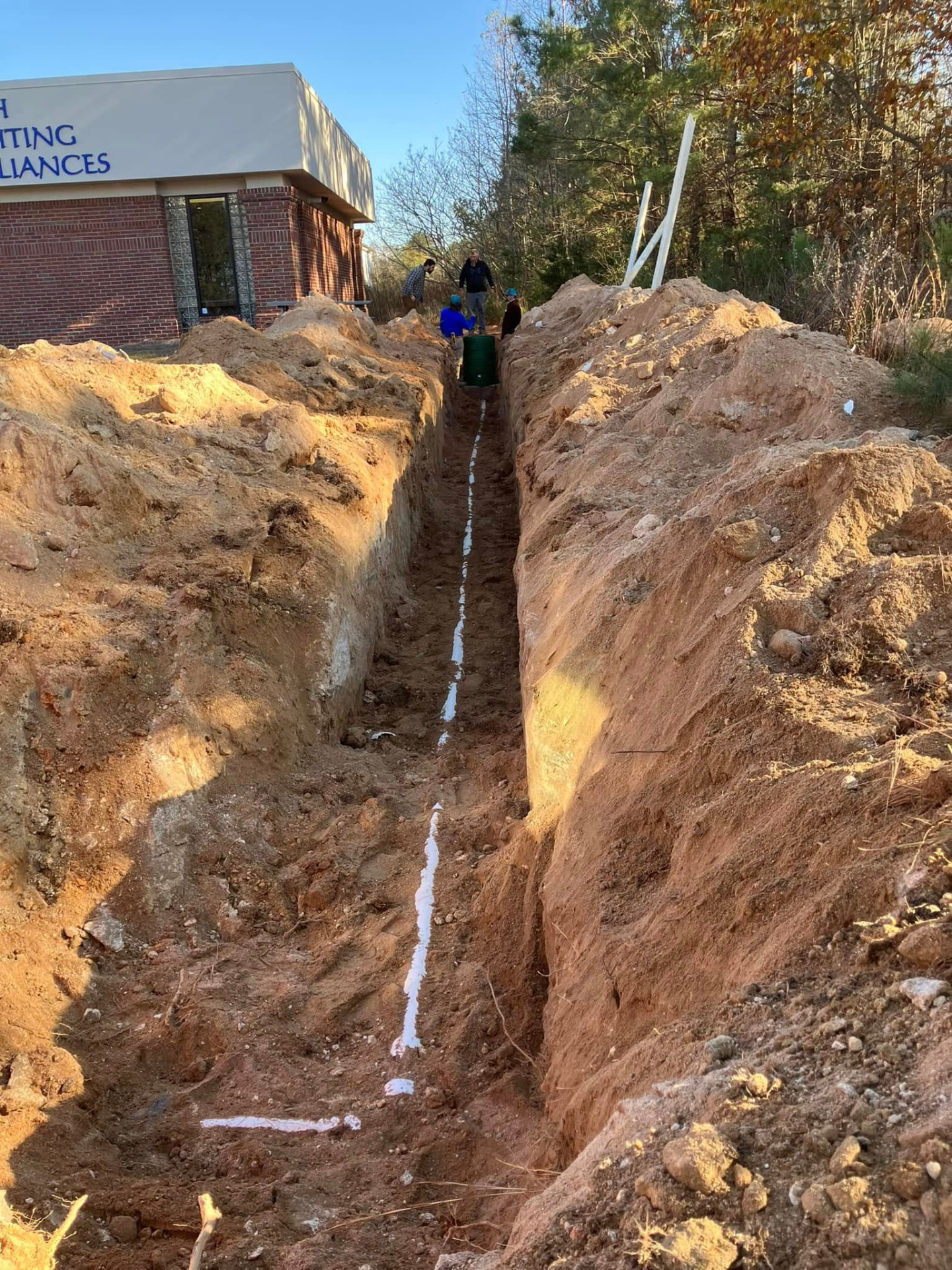EMS crew working in a deep excavated trench for sewer line installation