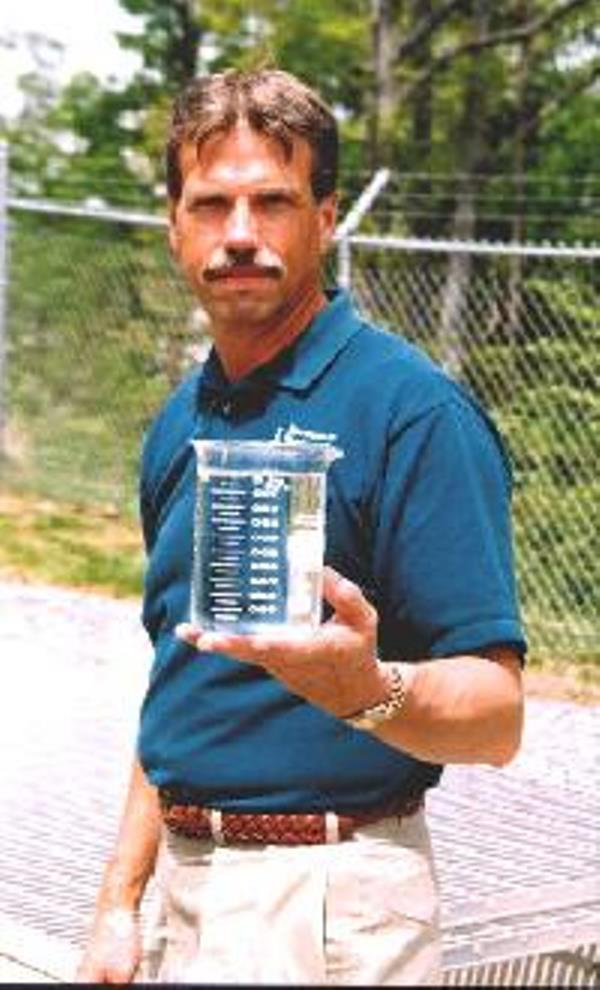 John H. Evans, founder of EMS, holding a clear water sample in a laboratory beaker.
