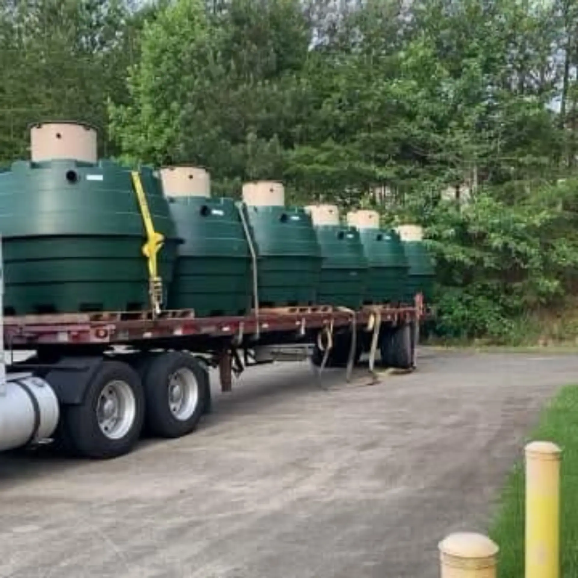 Flatbed trailer loaded with green Orenco tanks staged for delivery