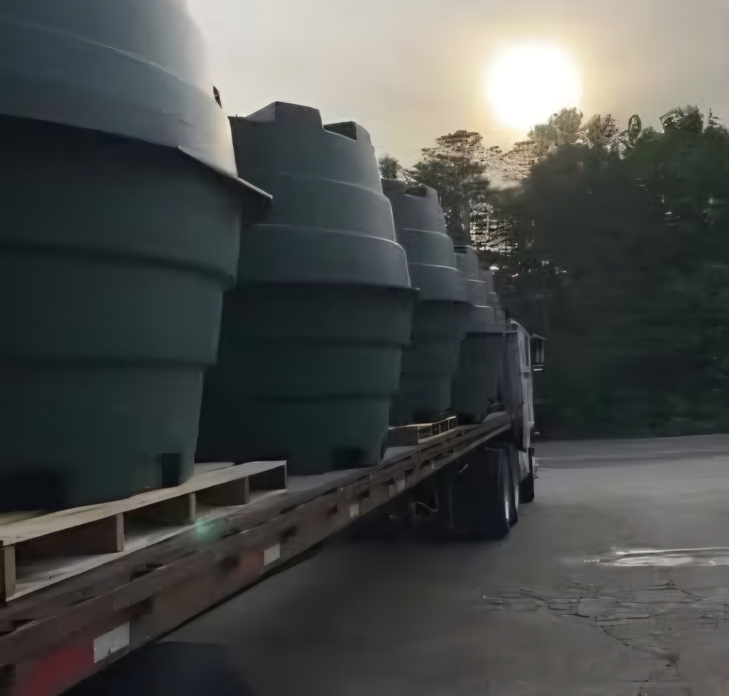 Flatbed trailer loaded with fiberglass tanks leaving the EMS yard at sunrise